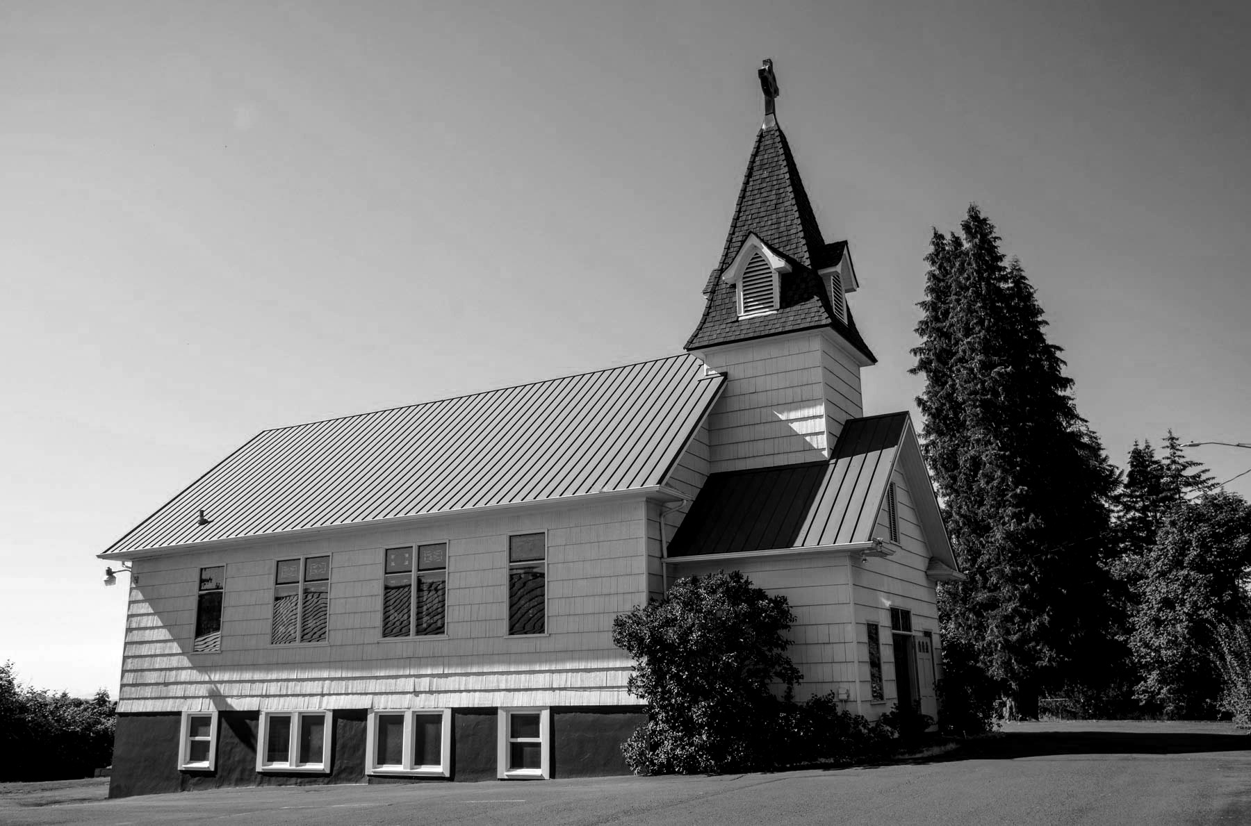 Beavercreek United Church of Christ in black and white on a sunny day, the church has stain glass windows and a tall steeple toward the front of the church